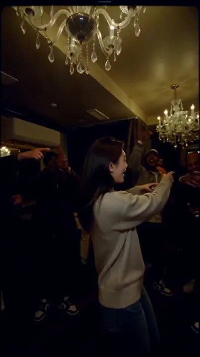 The room: A crowded party under a warm chandelier, friends cheering on both sides.